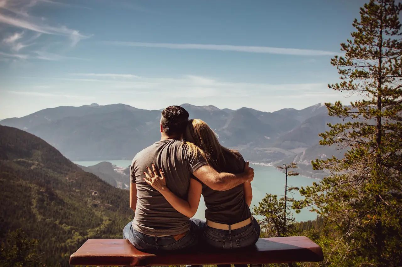 Couple embracing on a bench, overlooking scenic mountains and lake.